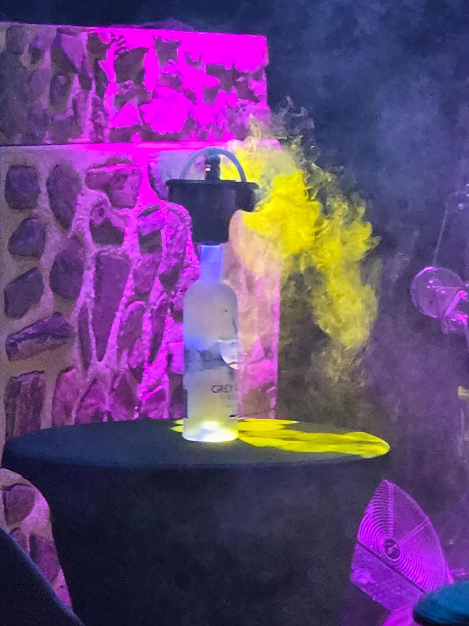 Dispositif sur une bouteille diffusant de la fumée dans une ambiance lumineuse violette et jaune